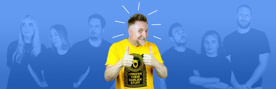 A man in a yellow t-shirt in front of a blue background giving a thumbs up